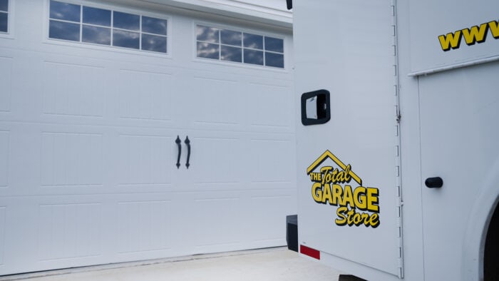 A side view captures a white garage door alongside a delivery van featuring "The Total Garage Store" logo and partial website URL. Their expertise in garage door replacement and installation is evident, ensuring quality service for all your needs.